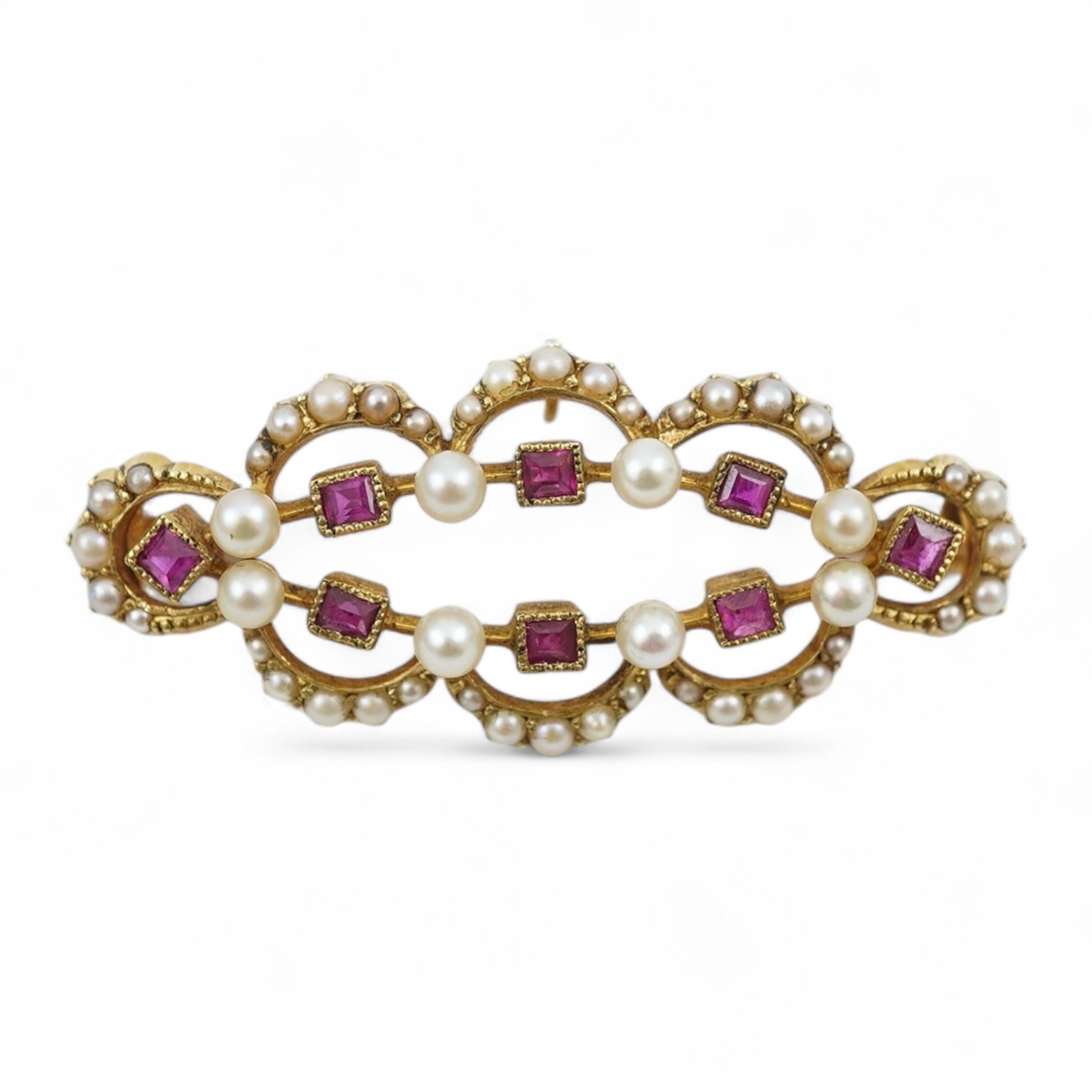 An Edwardian 15ct, ruby and seed pearl cluster set brooch, 33mm, with safety chain, gross weight 4.1 grams.